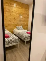 Zona de armario abierta en pared de madera con perchas y banco, junto a una cama con manta de corazones